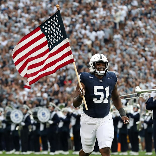 A Penn State football player carries the American flag onto the field at Beaver Stadium.