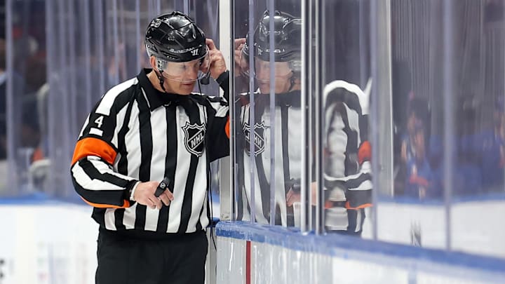 Mar 24, 2025; Elmont, New York, USA; NHL referee Wes McCauley (4) puts on a headset for a video review of a disallowed Islanders goal during the third period between the New York Islanders and the Columbus Blue Jackets at UBS Arena. Mandatory Credit: Brad Penner-Imagn Images