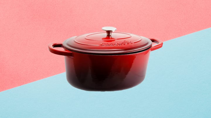 Crock Pot Artisan Seven-Quart Oval Enameled Cast Iron Dutch Oven in red against pink and blue background.