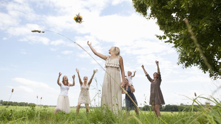 Bride throws wedding bouquet to bridesmaids behind her in a grassy field