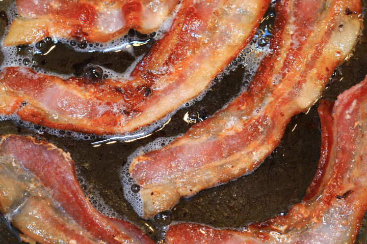 strips of bacon sizzling in a pan 