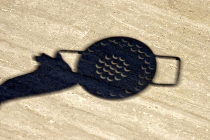Crescent shadows of partial solar eclipse viewed through a colander.