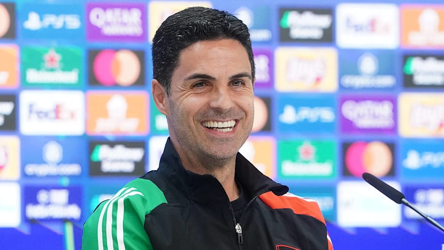 Mikel Arteta grinning widely at an Arsenal press conference.