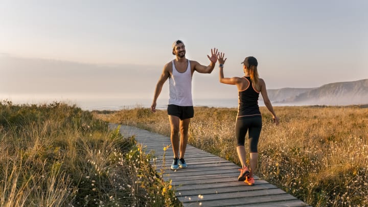 A fit man and woman high-five on a boardwalk in the golden hour