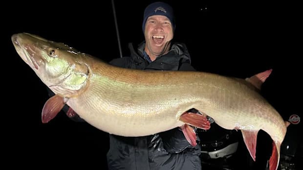 Art Weston at night on Lake Mille Lacs, smiling and holding a giant, 57.5-inch world-record muskie.