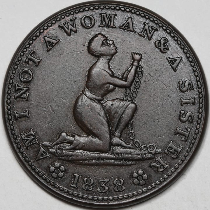 a dark metal coin with the year 1838, the words 'AM I NOT A WOMAN AND A SISTER', and a kneeling woman in chains