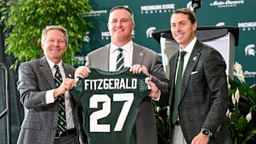 Michigan State football's new coach Pat Fitzgerald, center, holds up a jersey with MSU president Kevin Guskiewicz, left, and athletic director J Batt, right, during Fitzgerald's introductory press conference on Tuesday, Dec. 2, 2025, at the Tom Izzo Football Building in East Lansing.