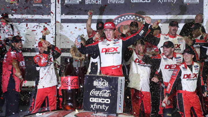 Harrison Burton climbs out of the no. 21 Ford as the crew showers him with Coke Zero Sugar in Victory Lane, Saturday August 24, 2024 after winning the Coke Zero Sugar 400 at Daytona International Speedway.