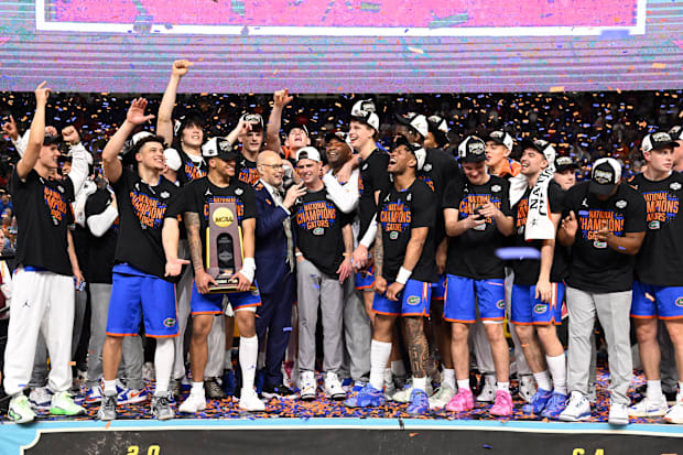 Florida coaches and players celebrate on stage with the NCAA tournament trophy and confetti falling around them