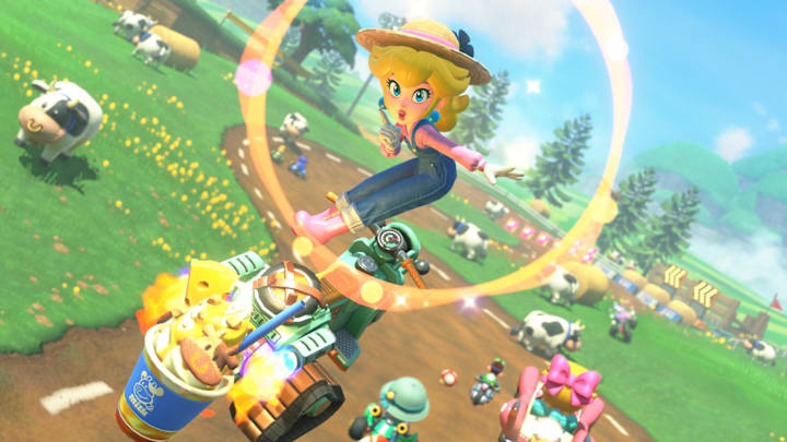 Peach wearing a farmer's outfit doing a trick on her bike while driving through a field of cows.