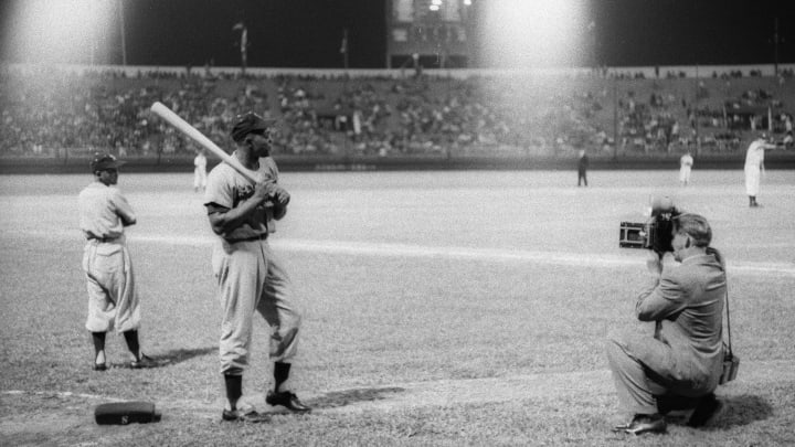 Willie Mays stands on deck as a photographer crouches in front of him.