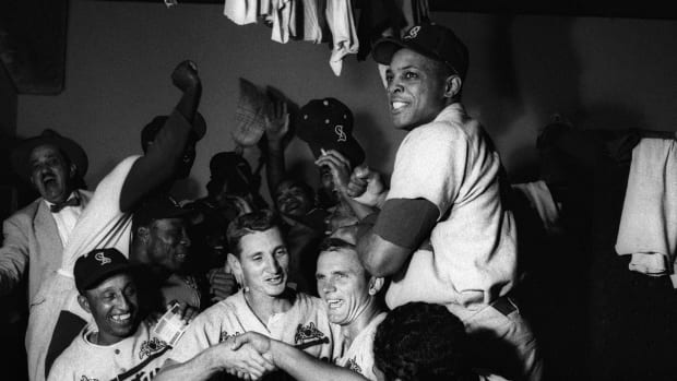 Willie Mays sits on top of a ddugout bench as teammates crowd below him