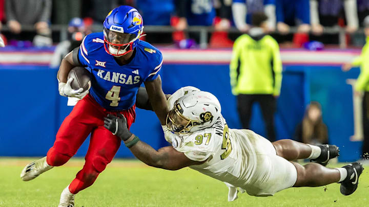 Nov 23, 2024; Kansas City, Missouri, USA;  Kansas running back Devin Neal (4) maneuvers past a diving during the Colorado defensive tackle Chidozie Nwankwo (97) in the 4th quarter between the Kansas Jayhawks and the Colorado Buffaloes at GEHA Field at Arrowhead Stadium. 
