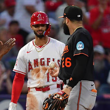Angels left fielder Matthew Lugo (15) is handed the ball by Baltimore Orioles third baseman Emmanuel Rivera (26) after hitting an RBI triple for his first major league hit during the fourth inning at Angel Stadium. Mandatory Credit: Gary A. Vasquez-Imagn Images