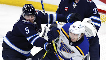 Apr 7, 2025; Winnipeg, Manitoba, CAN;  Winnipeg Jets defenseman Luke Schenn (5) checks St. Louis Blues left wing Jake Neighbours (63) in front of Winnipeg Jets goaltender Connor Hellebuyck (37) in the third period at Canada Life Centre. Mandatory Credit: James Carey Lauder-Imagn Images