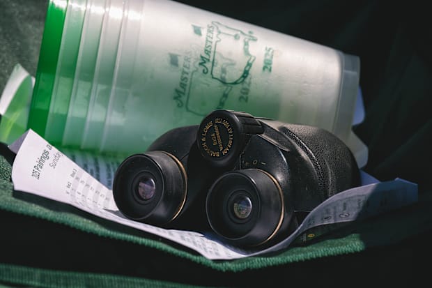 A close-up of a pair of binoculars and a stack of five 2025 Masters cups.