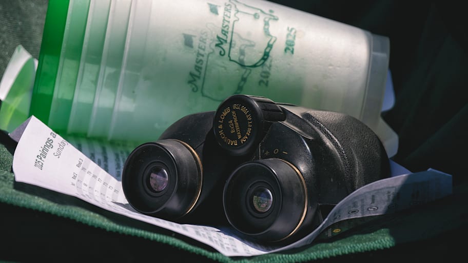 A close-up of a pair of binoculars and a stack of five 2025 Masters cups.