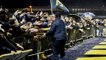 Braving the rain, University of Michigan fans lined up and reach over barriers to greet UM head