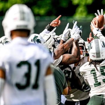 Michigan State defensive players huddle around the ball during the first day of football camp on Tuesday, July 30, 2024, in East Lansing.