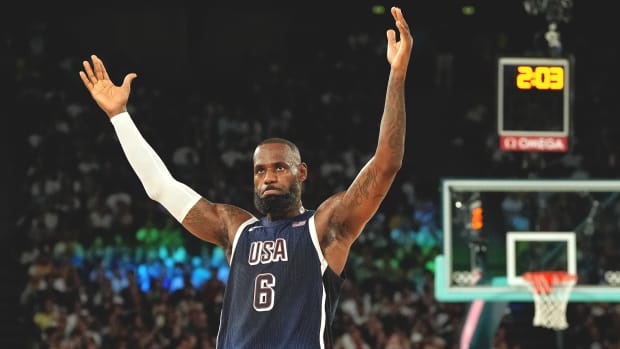 Team USA basketball player LeBron James stands with both arms outstretched into the air.