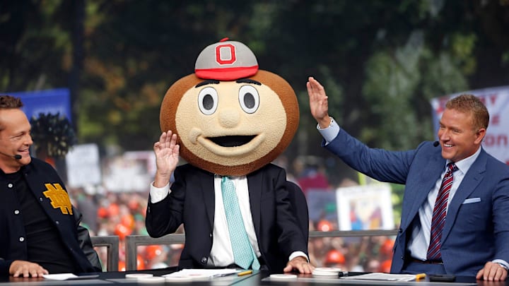 ESPN's Lee Corso, center, waves his hand after putting the Ohio State Buckeyes mascot head on to end \"College GameDay\" Saturday at Notre Dame. To the left is actor Vince Vaughn, and to the right is ESPN's Kirk Herbstreit.