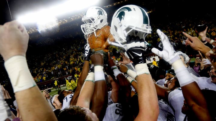 Michigan State players celebrate by raising the Paul Bunyan trophy, which has a Spartan helmet on,