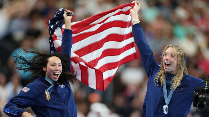 Torri Huske and Gretchen Walsh share the American flag and the podium after medaling in the 100-meter butterfly at the Paris Olympics.