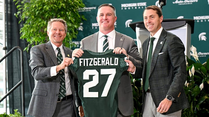 Michigan State football's new coach Pat Fitzgerald, center, holds up a jersey with MSU president Kevin Guskiewicz, left, and athletic director J Batt, right, during Fitzgerald's introductory press conference on Tuesday, Dec. 2, 2025, at the Tom Izzo Football Building in East Lansing.