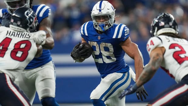 Colts running back Jonathan Taylor (blue jersey; white helmet/pants) looks for room to run with the football during a play. 