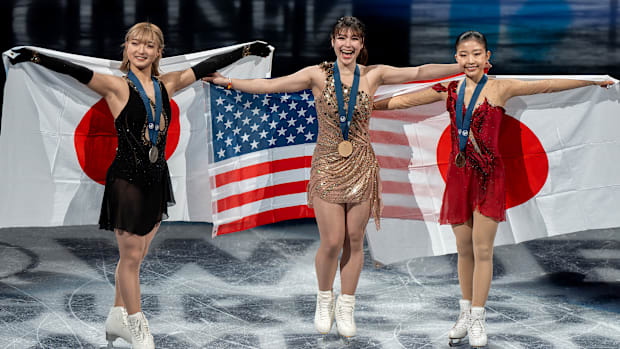 Alysa Liu (center), Kaori Sakamoto (left) and Mone Chiba (right) pose while holding their nation's flags after skating.