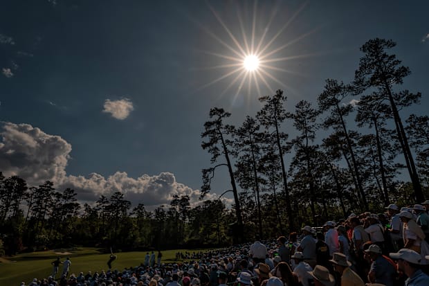 The sun shines down as patrons watch golfers hit tee shots at the par-3, 12th hole.