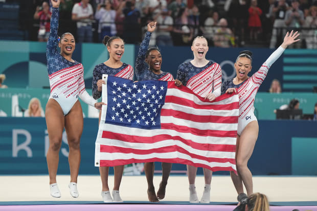 The U.S. women's gymnastics team celebrates with an American flag after winning gold in the team final at the Paris Olympics.