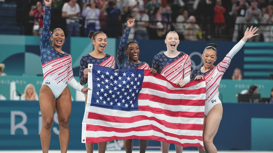 The U.S. women's gymnastics team celebrates with an American flag after winning gold in the team final at the Paris Olympics.