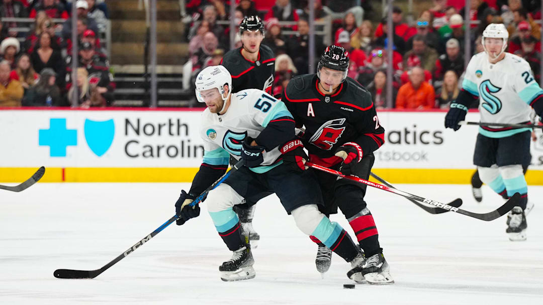 Dec 3, 2024; Raleigh, North Carolina, USA;  Carolina Hurricanes center Sebastian Aho (20) checks Seattle Kraken center Shane Wright (51) off the puck during the second period at Lenovo Center. Mandatory Credit: James Guillory-Imagn Images