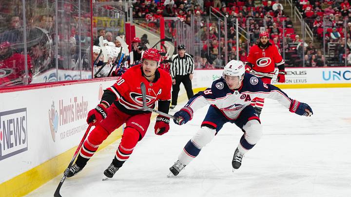 Jan 23, 2025; Raleigh, North Carolina, USA;  Carolina Hurricanes center Sebastian Aho (20) and Columbus Blue Jackets defenseman Zach Werenski (8) chase after the puck during the first period at Lenovo Center. Mandatory Credit: James Guillory-Imagn Images