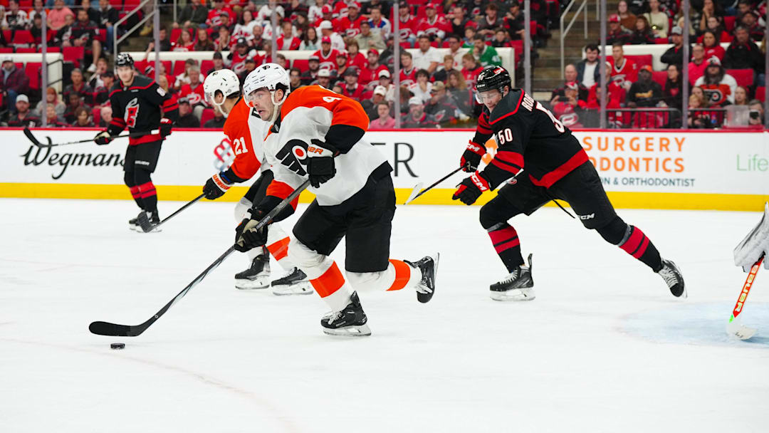 Nov 5, 2024; Raleigh, North Carolina, USA;  Philadelphia Flyers defenseman Jamie Drysdale (9) skates out of the defensive zone with the puck past Carolina Hurricanes left wing Eric Robinson (50) during the first period at Lenovo Center. Mandatory Credit: James Guillory-Imagn Images