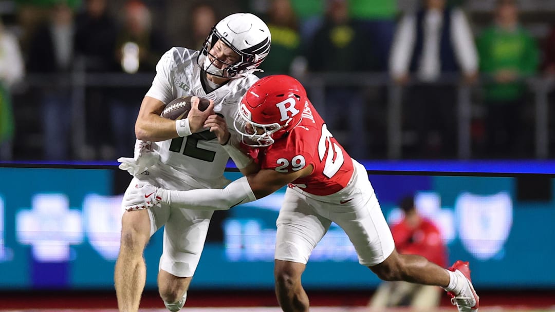 Oct 18, 2025; Piscataway, New Jersey, USA;  Oregon Ducks quarterback Brock Thomas (12) is tackled by Rutgers Scarlet Knights defensive back Sebastian Jusma (29) during the second half at SHI Stadium. Mandatory Credit: Vincent Carchietta-Imagn Images