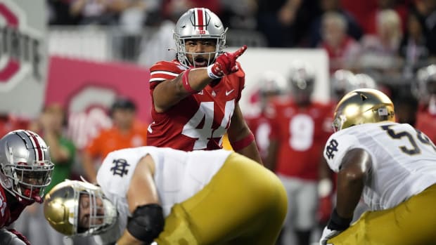 Football player points to quarterback on defense before play.