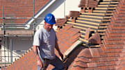 Roof tiler fixing hip bonnet tiles to roof of detached house.