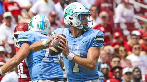 A football player wearing a white helmet with a green logo and blue jersey with white numbers holds the football. 