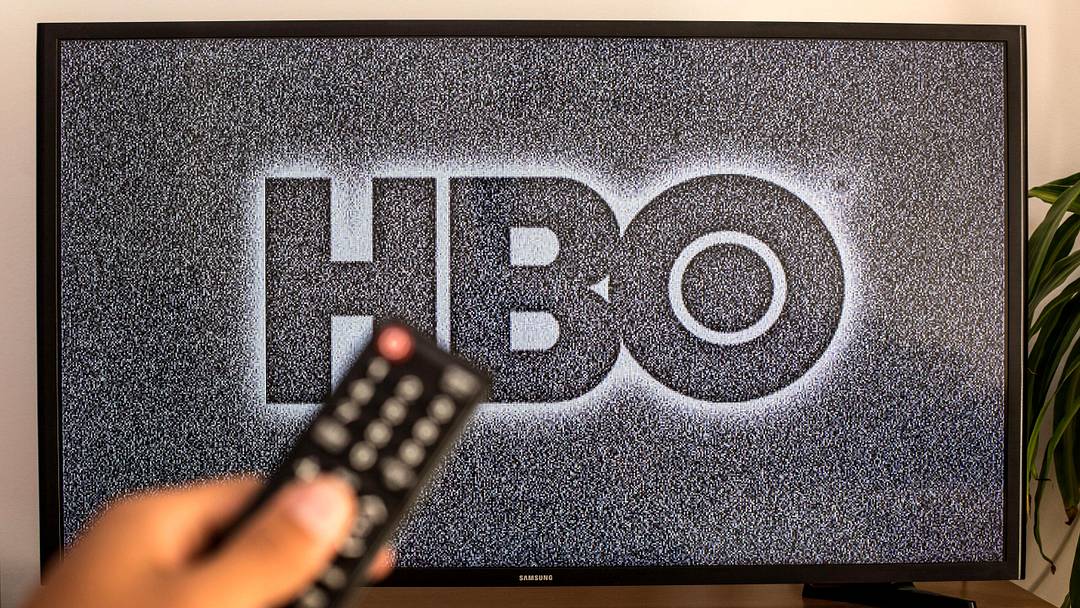 SPAIN – 2021/07/13: In this photo illustration a close-up of a hand holding a TV remote control seen displayed in front of the HBO logo on a tv in the background. (Photo Illustration by Thiago Prudencio/SOPA Images/LightRocket via Getty Images)