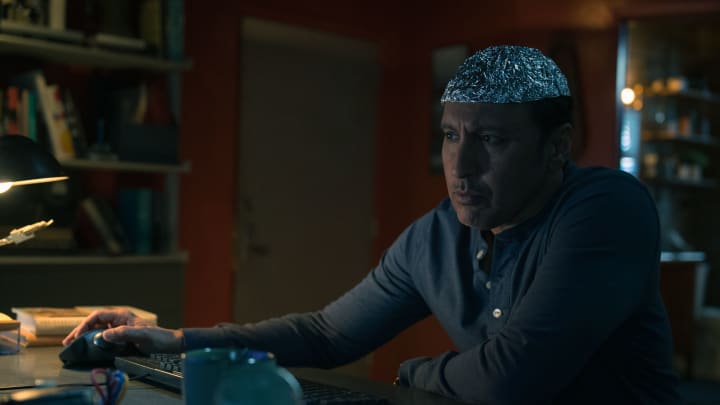 Ben Shakir (Aasif Mandvi) wears a tinfoil hat while reviewing footage on his computer