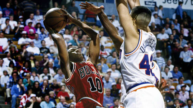 A basketball player wearing a white uniform defending another basketball player wearing a red uniform.