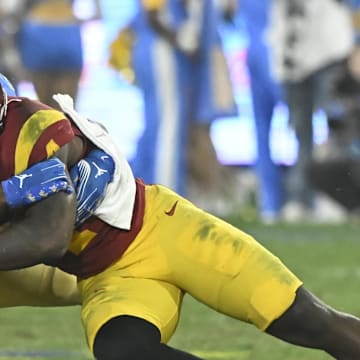 Nov 23, 2024; Pasadena, California, USA; USC Trojans running back Woody Marks (4) tries to break a tackle by UCLA Bruins linebacker Jalen Woods (17) during the third quarter at the Rose Bowl. Mandatory Credit: Robert Hanashiro-Imagn Images