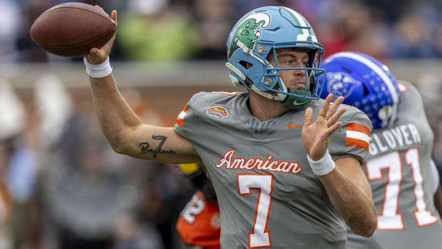 A football player prepares to throw the ball wearing a blue helmet with green logo, and grey jersey with white number.