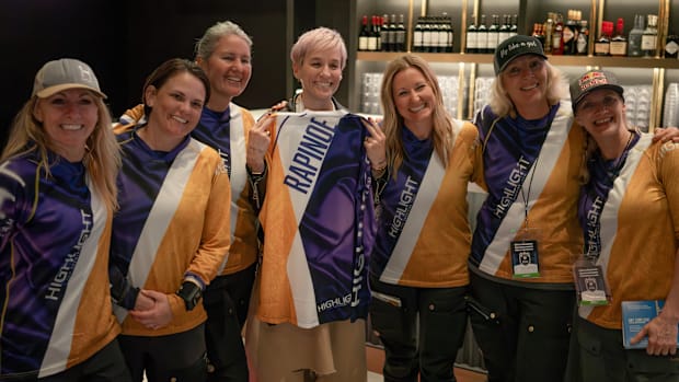 Six members of the Highlight Pro Skydiving Team wearing their yellow and purple uniform with Megan Rapinoe holding hers.