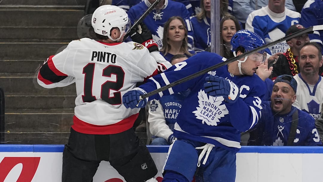 Apr 20, 2025; Toronto, Ontario, CAN; Toronto Maple Leafs forward Auston Matthews (34) checks Ottawa Senators forward Shane Pinto (12) along the boards during the first period of game one of the first round of the 2025 Stanley Cup Playoffs at Scotiabank Arena. Mandatory Credit: John E. Sokolowski-Imagn Images