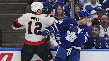 Apr 20, 2025; Toronto, Ontario, CAN; Toronto Maple Leafs forward Auston Matthews (34) checks Ottawa Senators forward Shane Pinto (12) along the boards during the first period of game one of the first round of the 2025 Stanley Cup Playoffs at Scotiabank Arena. Mandatory Credit: John E. Sokolowski-Imagn Images