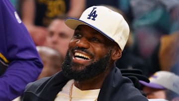 Oct 5, 2025; San Francisco, California, USA;  Los Angeles Lakers forward LeBron James (23), wearing a Los Angeles Dodgers hat, smiles after watching his son, guard Bronny James (9), dunk a rebound against the Golden State Warriors in the third quarter at Chase Center. Mandatory Credit: David Gonzales-Imagn Images
