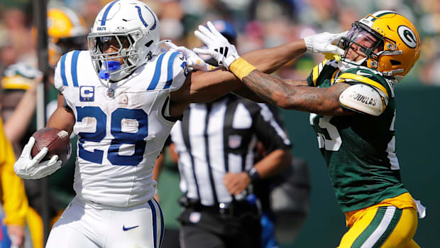 Colts running back Jonathan Taylor (white and blue uniform) stiff arms a defender in hot pursuit.